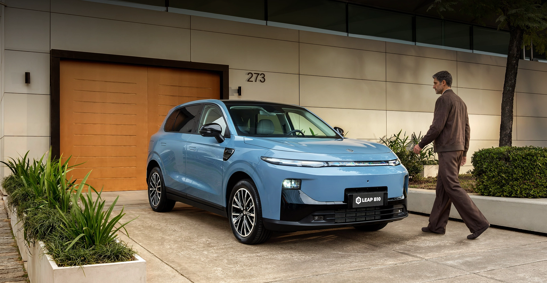 Autonomia de até 900 km Leapmotor B10 azul estacionado em frente a uma residência, com um homem caminhando em direção ao veículo.