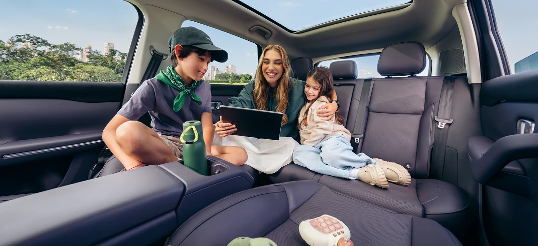 Banco traseiro de um Leapmotor com uma família de três pessoas sentadas, uma mulher no centro com um tablet em mãos, um homem e uma criança nas laterais, com troncos voltados levemente entre si.