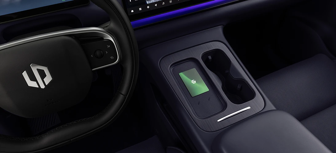 Console central do Leapmotor com superfície de carregamento por indução, smartphone posicionado sobre o ícone de bateria e porta-objetos ao redor.