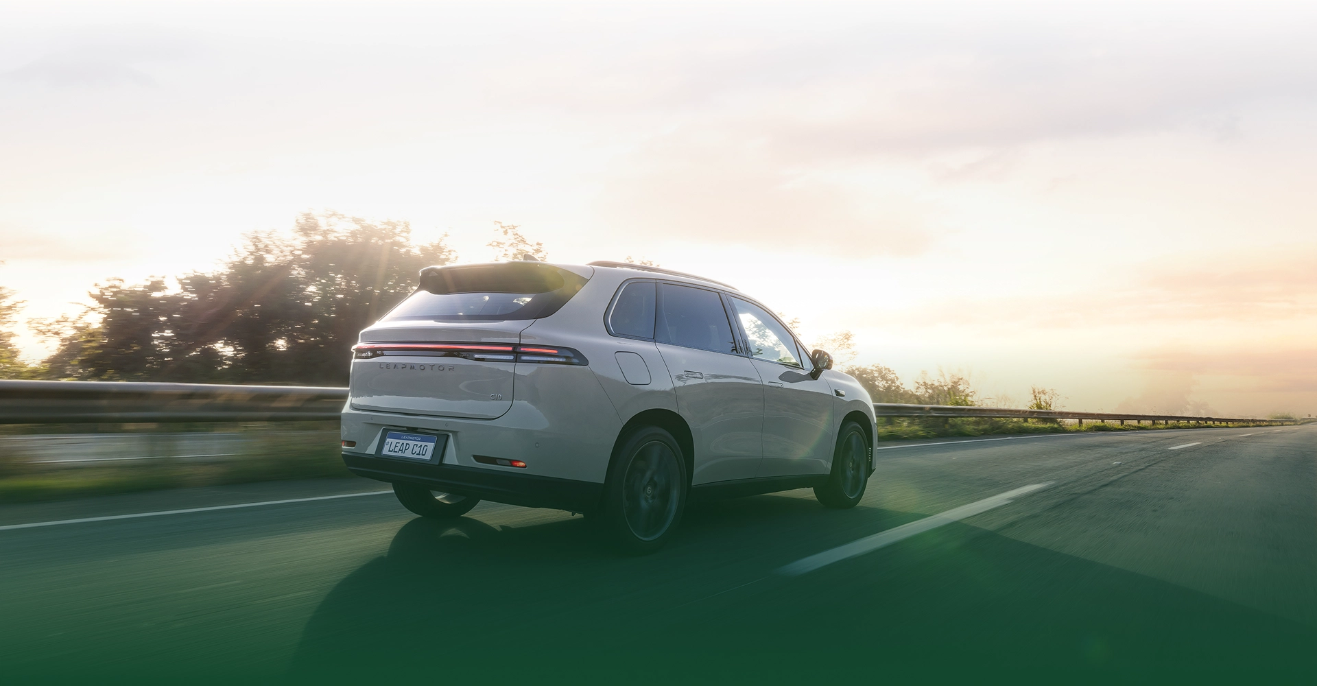 Vista traseira de um SUV Leapmotor branco em movimento sobre rodovia, com lanterna traseira em LED em faixa contínua com luz de fim de tarde ao fundo.